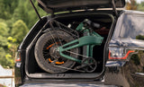 Green Engwe EP-2 3.0 Boost Electric bicycle folded and secured in the trunk of a black car with a blurred natural background