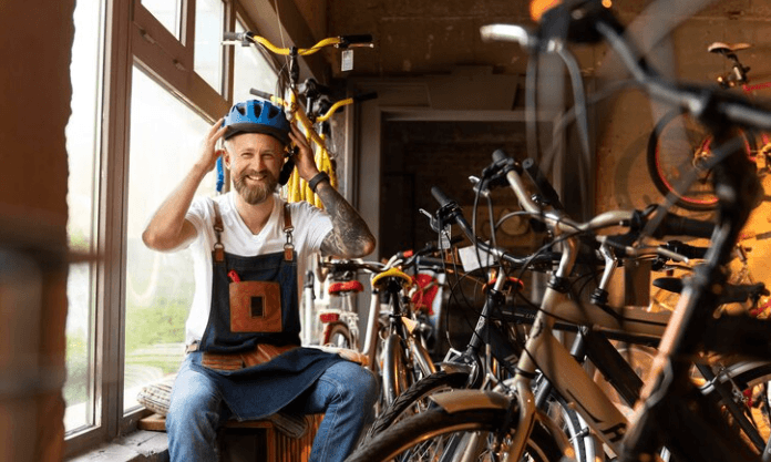 Electric bikes lined up in a bike store with a smiling man adjusting a helmet, indoor setting