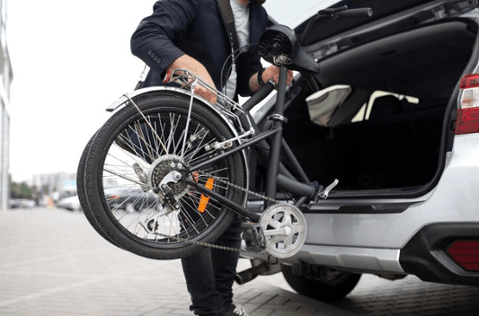 Folded black electric bike being loaded into a car trunk, side view, urban setting