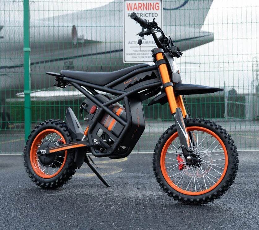 Riding Times GT54  off-road electric bike on a road with a fence and airplane in the background.